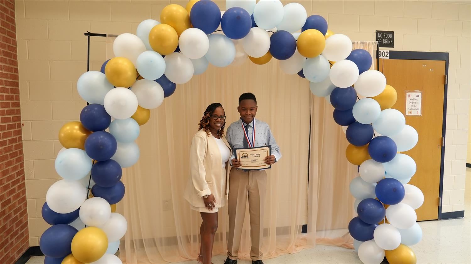 Proud mother taking a picture with her son under a balloon arch